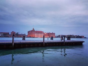 Stilt houses in sea against cloudy sky