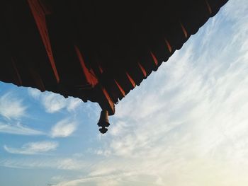 Low angle view of man hanging from roof against sky