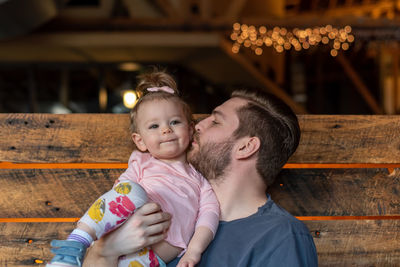 Father kissing cute daughter while sitting on bench