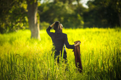 Rear view of young woman standing amidst grassy field