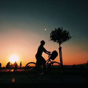 Silhouette woman riding bicycle against sky during sunset