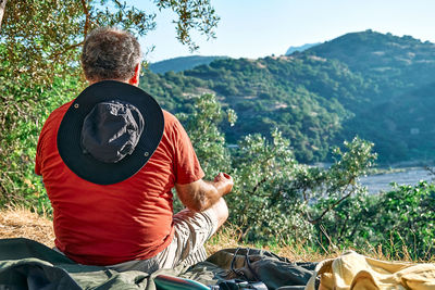 Tourist man resting in olive grove, meditating in front of mountain view or exercising outdoors. 