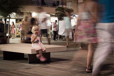 Blurred motion of people walking around girl in city