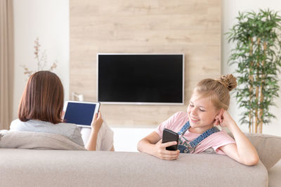 Woman using digital tablet while sitting by daughter on sofa at home