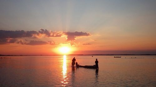 Silhouette people on sea against sky during sunset