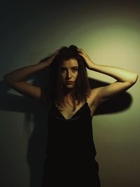 Portrait of young woman holding head against wall