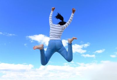 Rear view of woman jumping in mid-air against sky