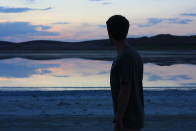 Rear view of silhouette man standing at beach against sky