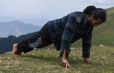 A indian young man with ponytail hair doing three finger push ups in the top of mountain