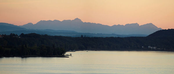 Scenic view of lake by mountains against sky during sunset