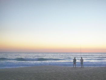 Silhouette people standing on beach against sky during sunset