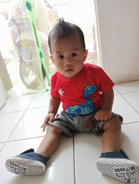 Portrait of cute girl sitting on tiled floor at home