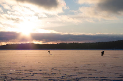 Silhouette people standing on frozen lake against sky during sunset