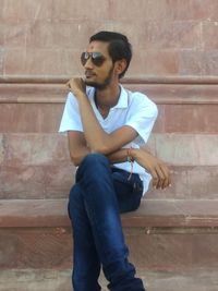 Young man wearing sunglasses sitting against wall