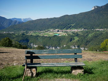 Bench in park by mountains against sky