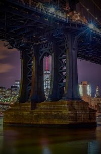 Low angle view of manhattan bridge over river in illuminated city at dusk