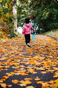 A girl is walking along a road strewn with leaves with kerosene lamp