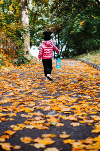 A girl is walking along a road strewn with leaves with kerosene lamp