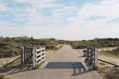 Open gate on footpath at beach against sky