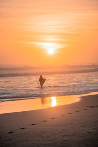 Surfer standing in sea during sunset