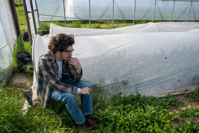 Young male farmer contemplates inside greenhouse by vegetable rows