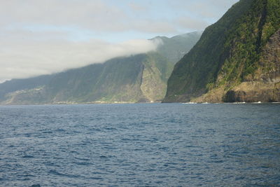 Scenic view of sea by mountain against sky