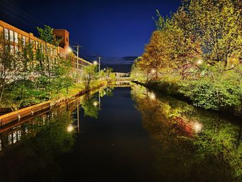 Illuminated building by lake against sky at night