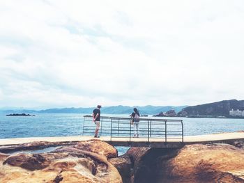 Rear view of people standing by sea against sky