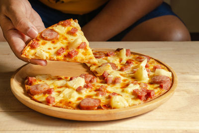 Close-up of hand holding pizza on table