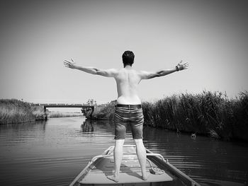 Rear view of shirtless man standing in lake against sky