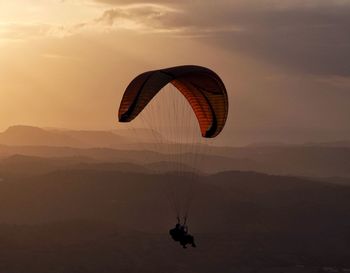 Silhouette people paragliding against sky during sunset