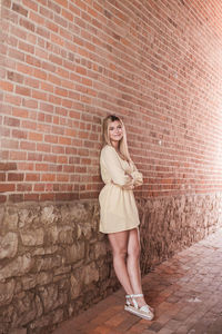 Portrait of a smiling young woman standing against brick wall