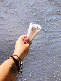 Cropped image of hand holding ice cream cone in front of wall