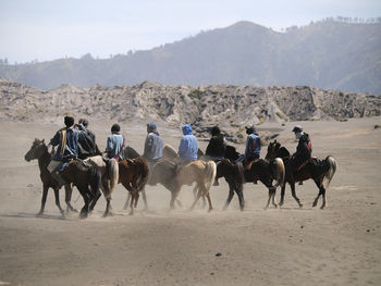 People riding horses on landscape against mountains