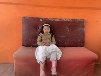 Girl with eyes closed sitting on sofa against wall