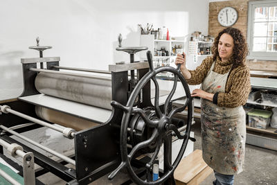 Female artist operating a manual vintage industrial printer.