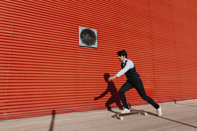 Businessman with longboard skateboarding on footpath by wall