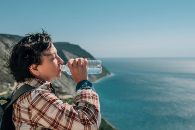 Side view of man photographing sea against clear sky