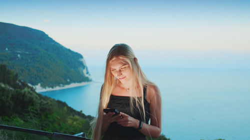 Young woman using mobile phone against sea