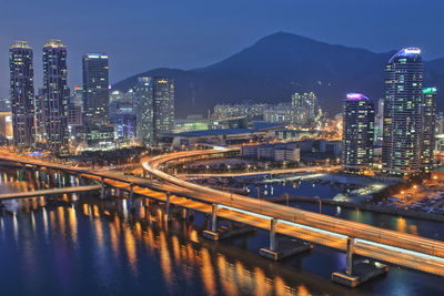 Illuminated bridge over river by buildings against sky at night