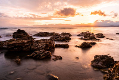 Rocks on sea shore against sky during sunset