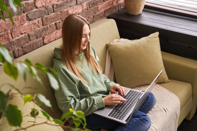 Young woman using laptop while sitting on sofa at home