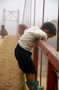 Side view of boy standing by railing