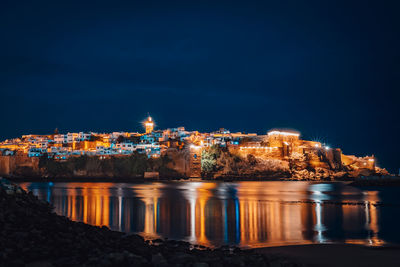 Illuminated city by river against sky at night