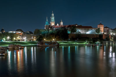 Illuminated buildings by river against sky at night