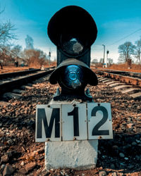 Information sign by railroad tracks against sky