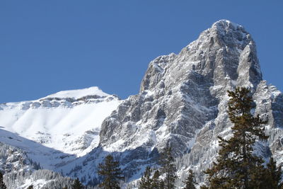 Low angle view of snowcapped mountains against clear blue sky