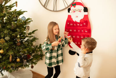 Rear view of siblings standing by christmas tree at home
