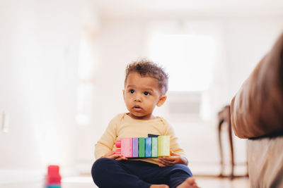 Cute boy looking away while sitting on floor at home