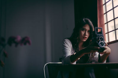 Portrait of young woman photographing through window at home